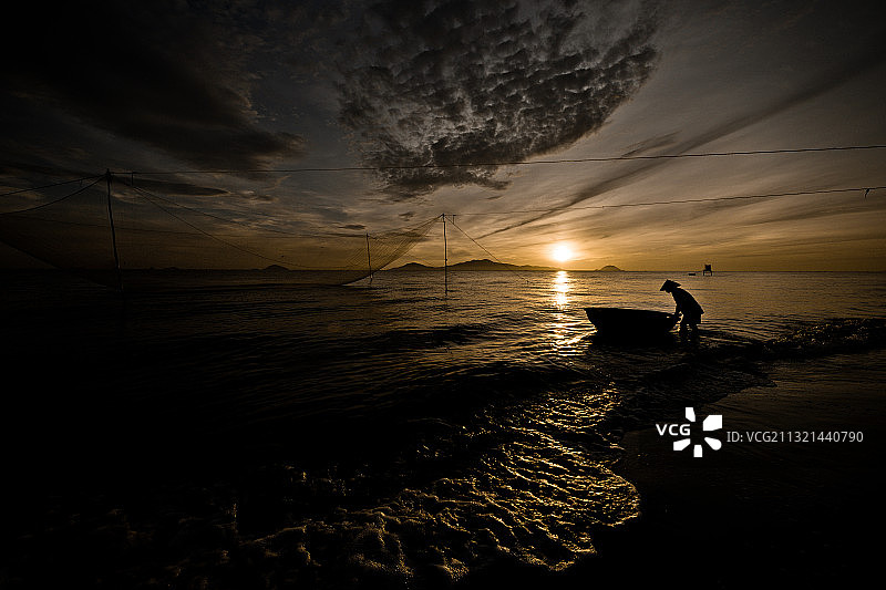 日落时分，越南老城，渔民在海上捕鱼的剪影图片素材
