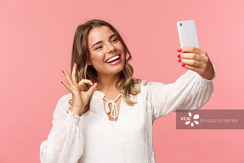 粉色背景下微笑的女人用手机的肖像图片素材