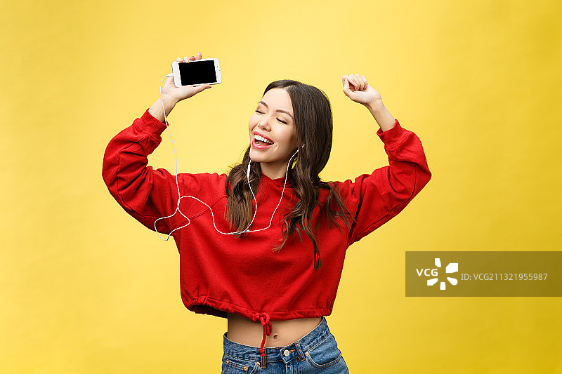 一个快乐的女孩用耳机在她的移动电子设备上听音乐图片素材