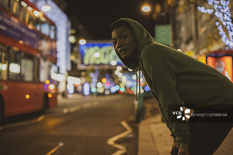 英国伦敦，年轻女性慢跑者在晚上等着穿过城市街道图片素材