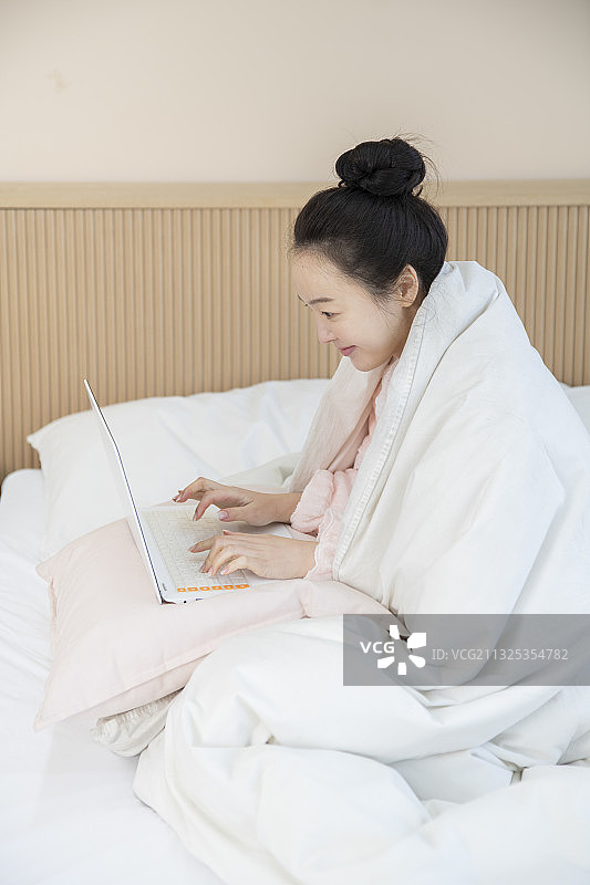 亚洲女人穿着睡衣在毯子下使用笔记本电脑图片素材