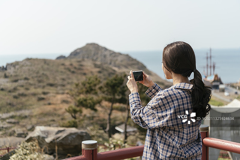 济州岛，一名女子站在栏杆旁用智能手机拍照图片素材