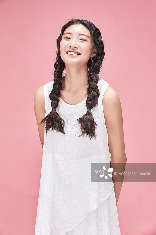 粉色背景前的身穿白色连衣裙的活力亚洲少女图片素材
