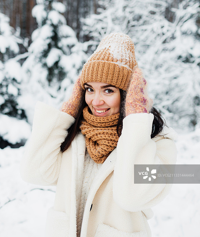 一个微笑的年轻女子在冬天靠着树站着的肖像图片素材