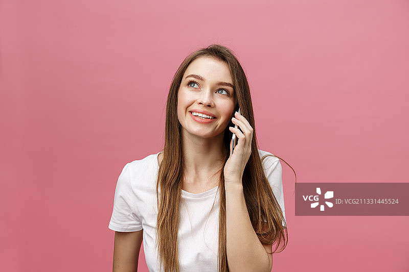微笑的年轻女子在粉红色的背景下讲手机图片素材