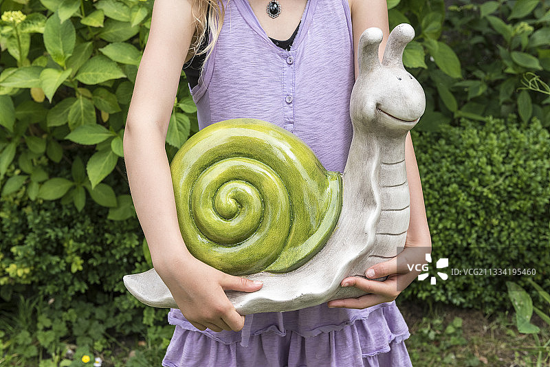 法国加来Pas de Calais的春天，一个女孩在花园里抱着一只装饰性的蜗牛图片素材