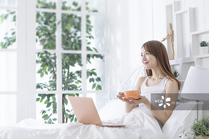 一位美女在卧室开心的喝咖啡及使用笔记本电脑图片素材