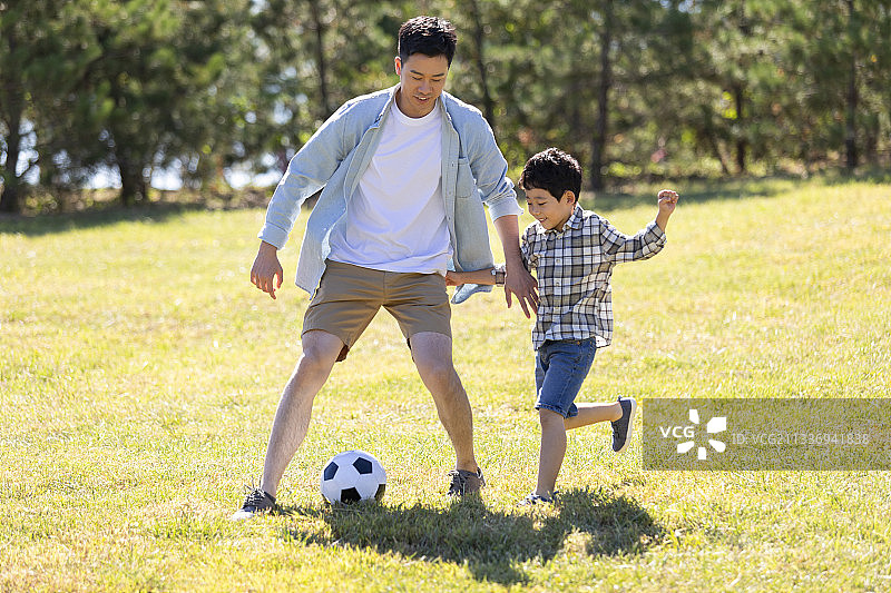 快乐的父子俩在草地上踢足球图片素材