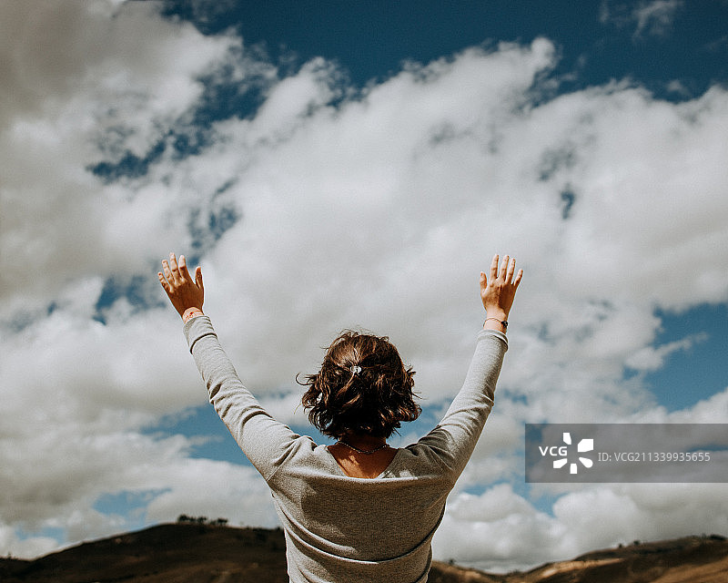 女子的后视图与手臂举起站在多云的天空，卡哈马卡，秘鲁图片素材