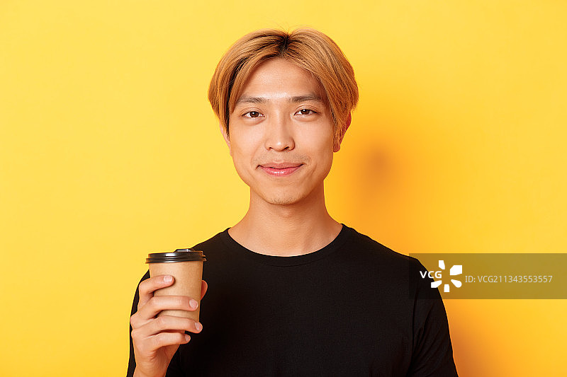 年轻男子拿着咖啡杯，背景是黄色的图片素材