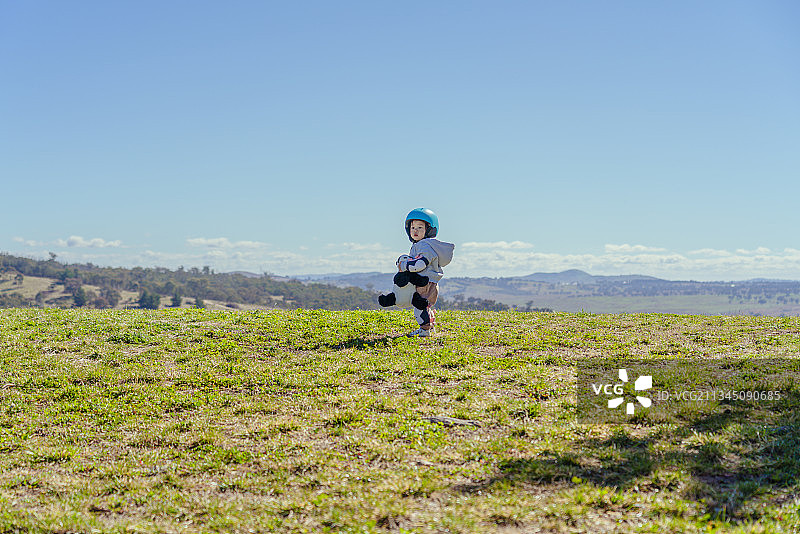山坡草坪上抱布偶熊的快乐头盔男孩图片素材