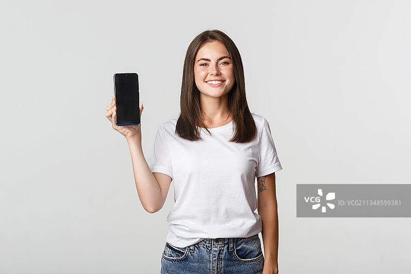 微笑的年轻女子的肖像显示手机在白色的背景图片素材