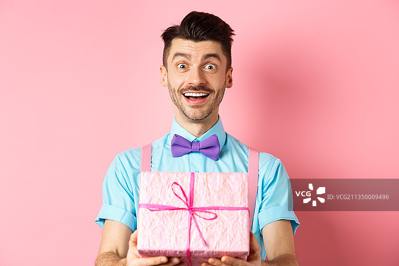 微笑的年轻人的肖像拿着礼物盒在粉红色的背景图片素材