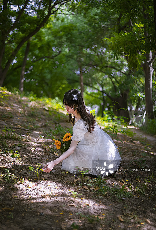 清晨树林里穿着白色连衣裙拿着花朵的女孩图片素材