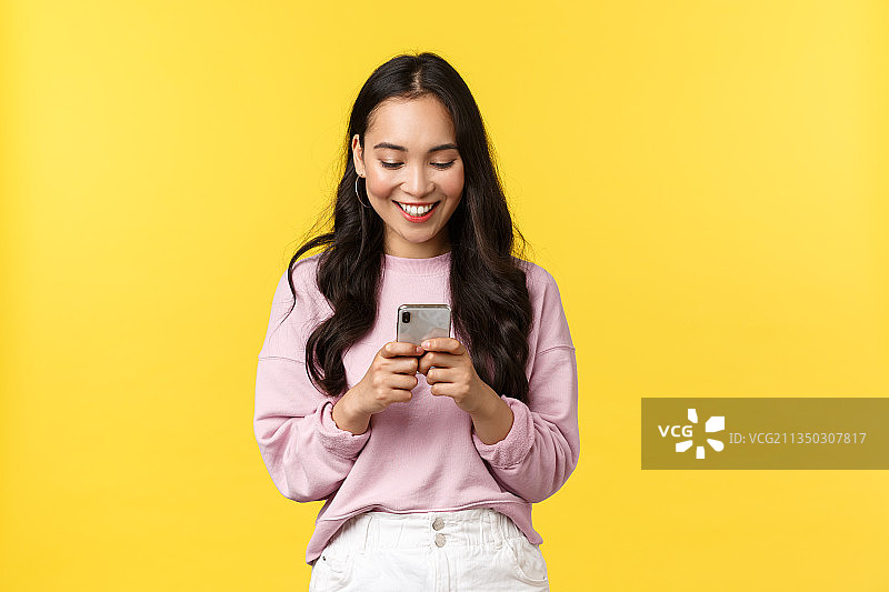 微笑的年轻女子在黄色背景下使用手机图片素材