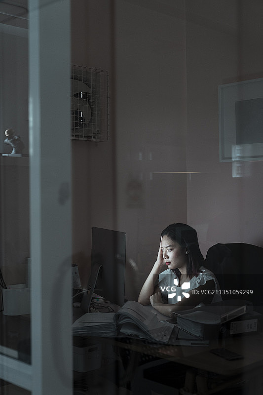 紧张的亚洲女人坐在办公室的电脑工作到午夜-加班的概念。图片素材