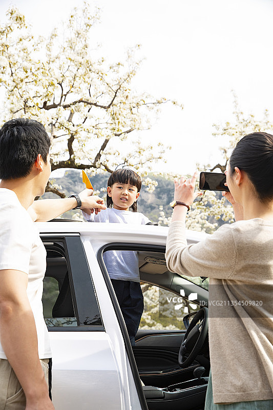 幸福的父母给从汽车天窗探出头来的儿子用手机拍照图片素材
