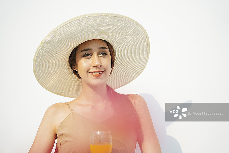 美丽迷人的深色女人戴着大帽子和橙汁在白色背景孤立的玻璃杯。图片素材