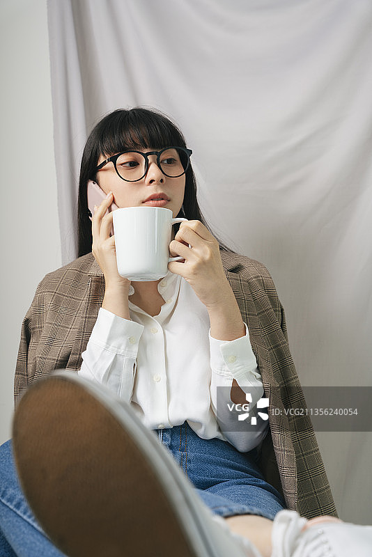 时尚肖像-美丽的亚洲泰国深色头发的女人穿着白衬衫戴着眼镜拿着一杯热咖啡和智能手机。图片素材