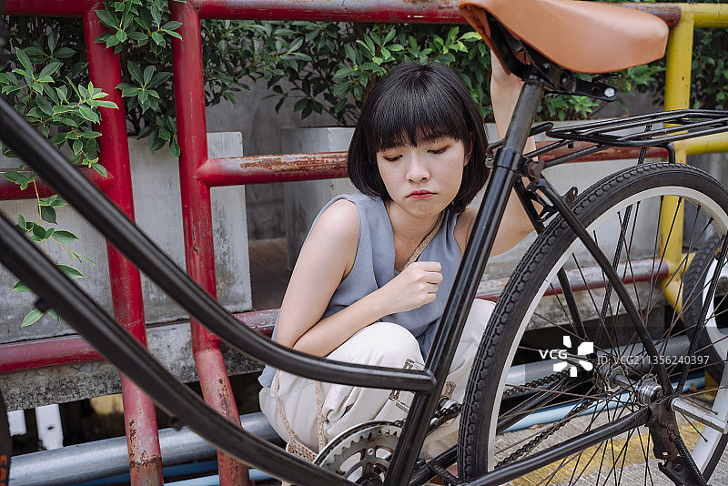 年轻的亚洲泰国女人坐在坏自行车旁边，心情沮丧，等待有人来修理它。图片素材