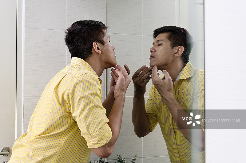 亚洲男子在镜子前检查面部痤疮问题。图片素材