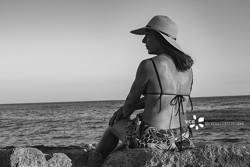 意大利塔兰托贝瓦尼亚的圣彼得罗，一名女子坐在沙滩上的岩石上，背靠着天空图片素材