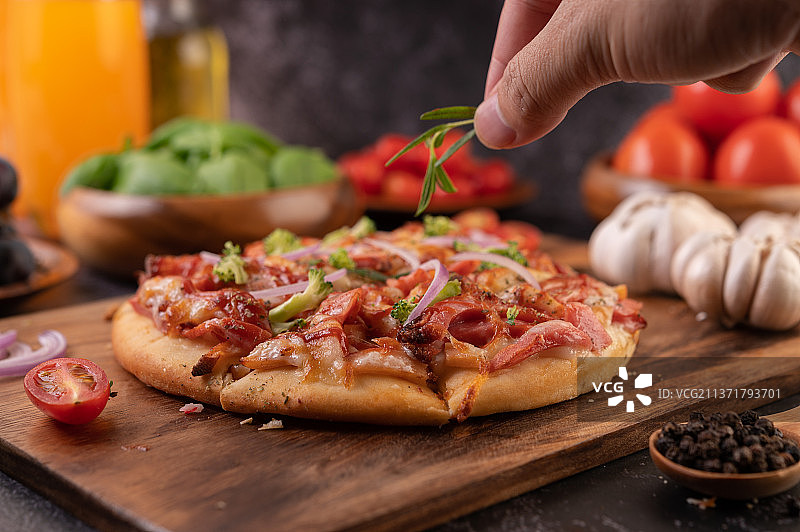 披萨放在木盘上，裁切披萨的人的手放在桌上图片素材