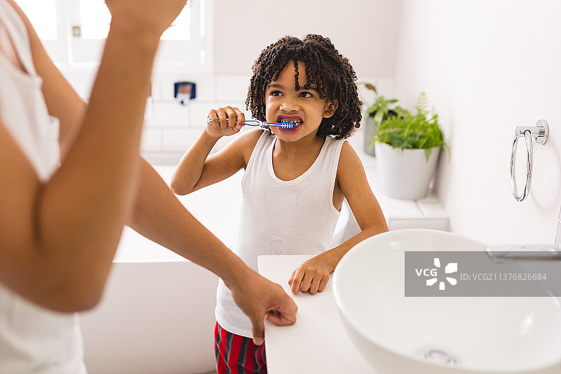 西班牙男孩刷牙时，看着父亲站在浴室的水槽旁图片素材