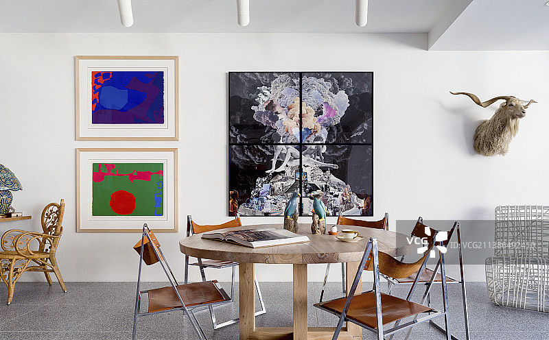 开放式客厅里的圆形木桌和镀铬皮革框架的复古椅子，墙上挂着现代艺术作品图片素材