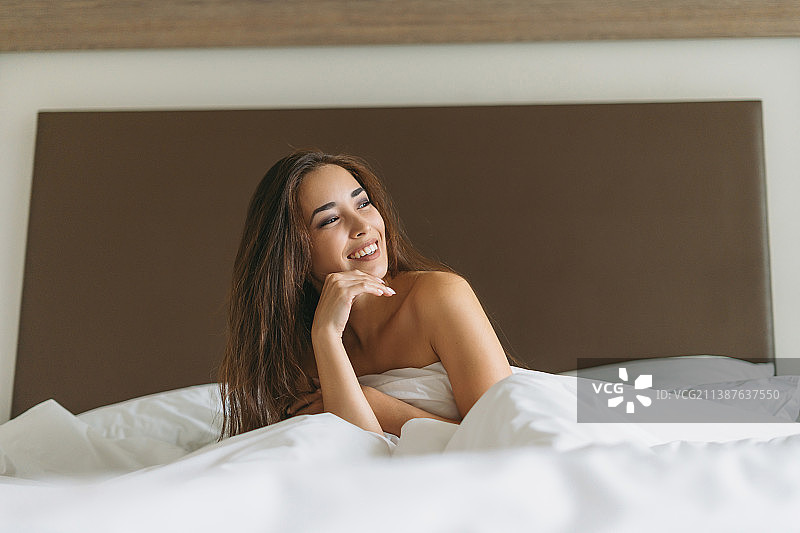 美丽的亚洲年轻女子长头发在床上与白色的被褥的酒店房间图片素材