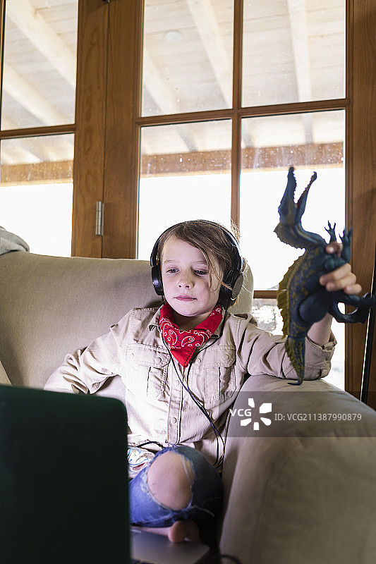 小男孩穿着狩猎装，戴着耳机在笔记本电脑上看电影图片素材