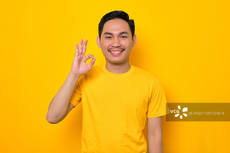 印度尼西亚，微笑的亚洲年轻男子做认可的手势与手指孤立的黄色背景图片素材