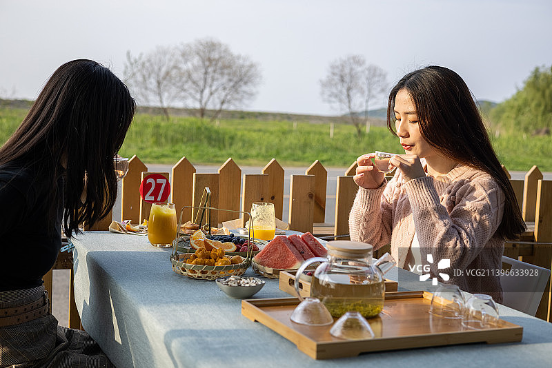春季夕阳下两个年轻女孩社交聚会举杯庆祝喝下午茶吃点心聊天图片素材