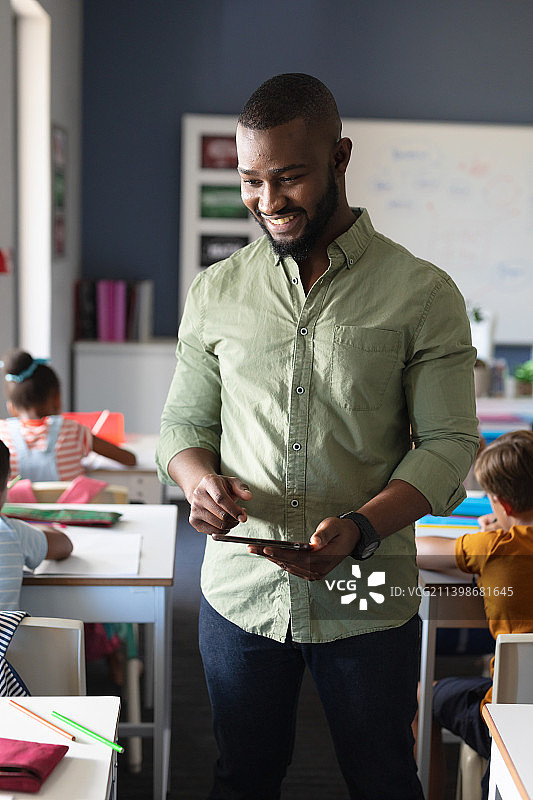 微笑的非洲裔美国年轻男老师拿着电子平板站在多种族学生旁边图片素材