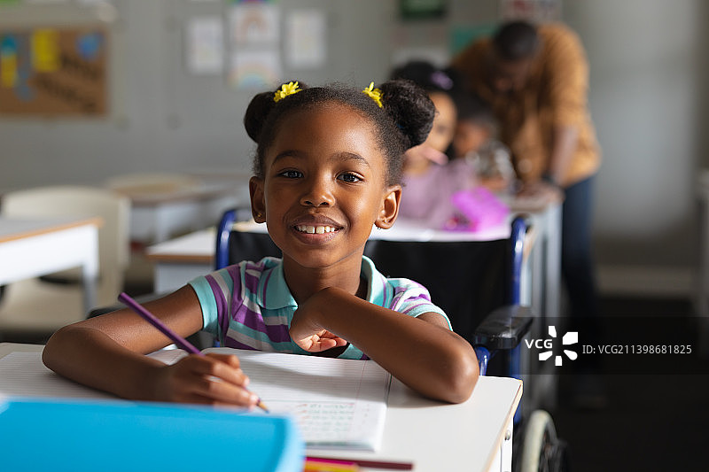 微笑的非洲裔美国小学女孩的肖像，坐在轮椅上学习的书桌图片素材