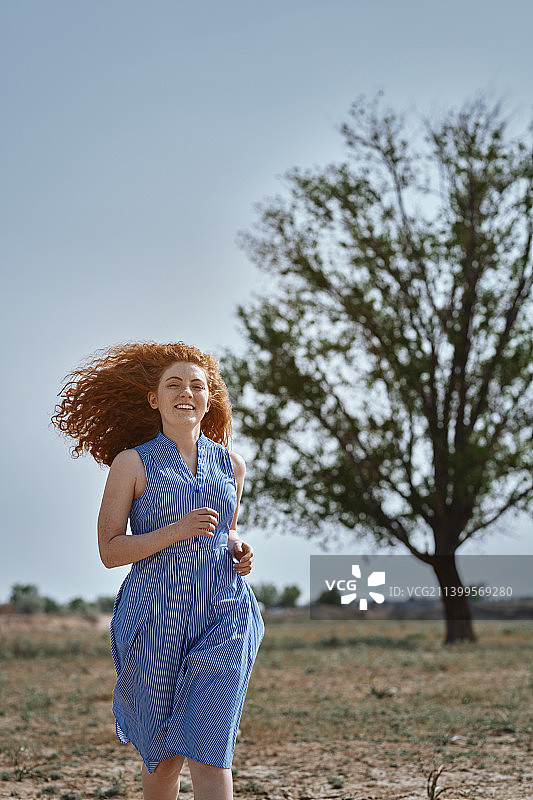 年轻的红发女子在一棵树旁奔跑，享受大自然图片素材