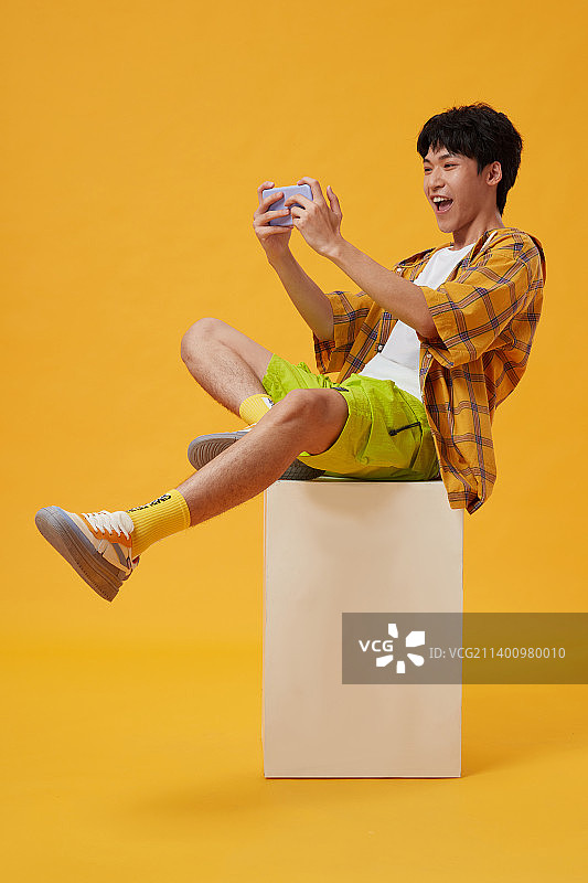 坐在木箱子上玩手机的年轻男孩图片素材