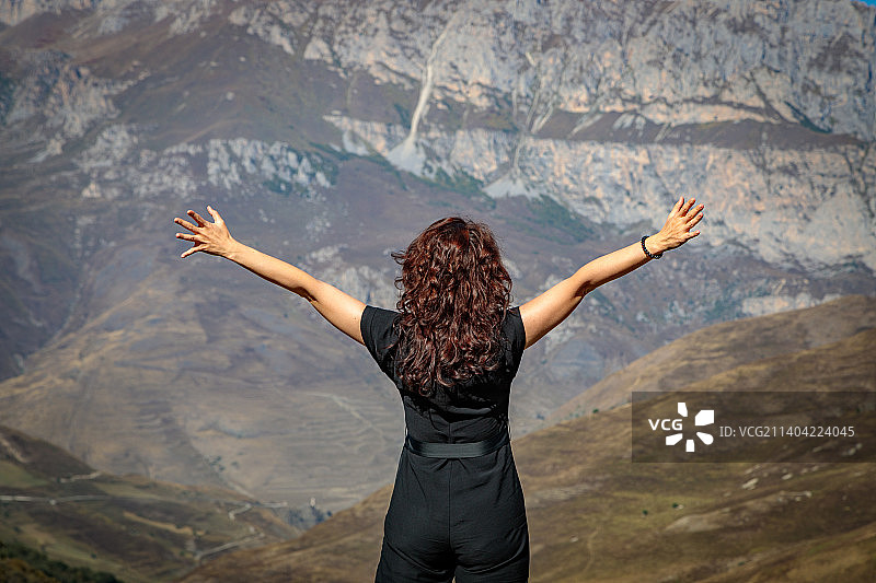 一个年轻的女人站在山顶上，张开双臂图片素材