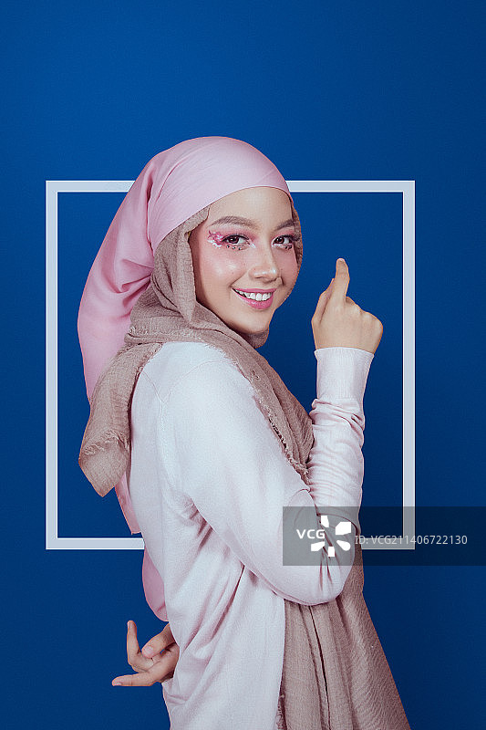 印度尼西亚巴东，蓝色背景下戴着头巾微笑的年轻女子的肖像图片素材