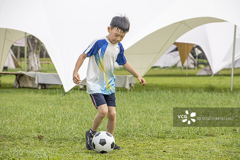 公园草地上的露营帐篷前踢足球的小男孩图片素材