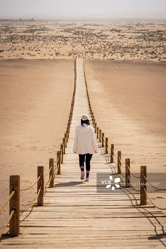 一个女孩走在独木桥上往沙漠的尽头中走去图片素材