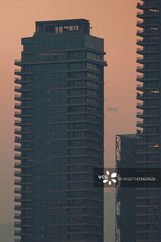 飞机飞过夕阳下的城市建筑图片素材