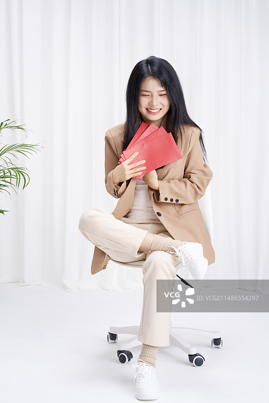 手拿手机与红包坐在椅子上的年轻女孩图片素材