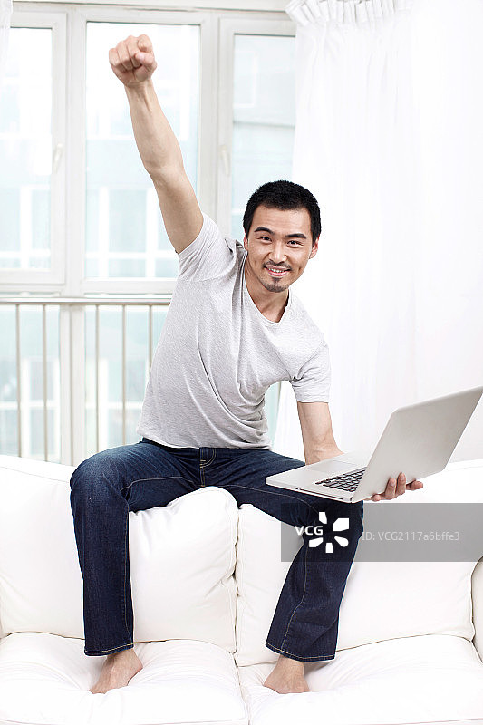 一个坐在白色沙发上用笔记本电脑的青年男士图片素材