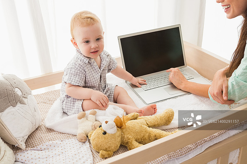 快乐的母亲使用笔记本电脑和她的儿子在家里的卧室图片素材