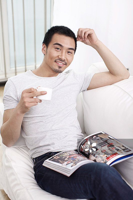 一个坐在白色沙发上看杂志的青年男士图片素材
