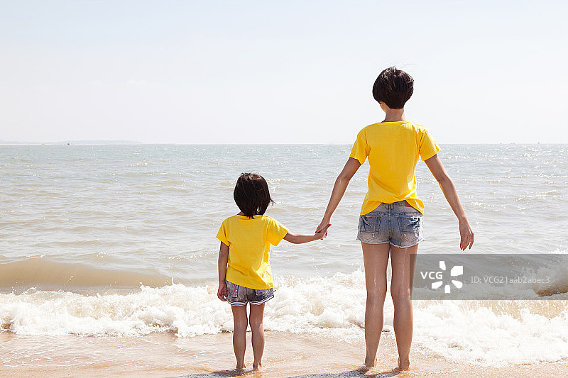 妈妈和女儿手牵手站在沙滩上面对大海图片素材