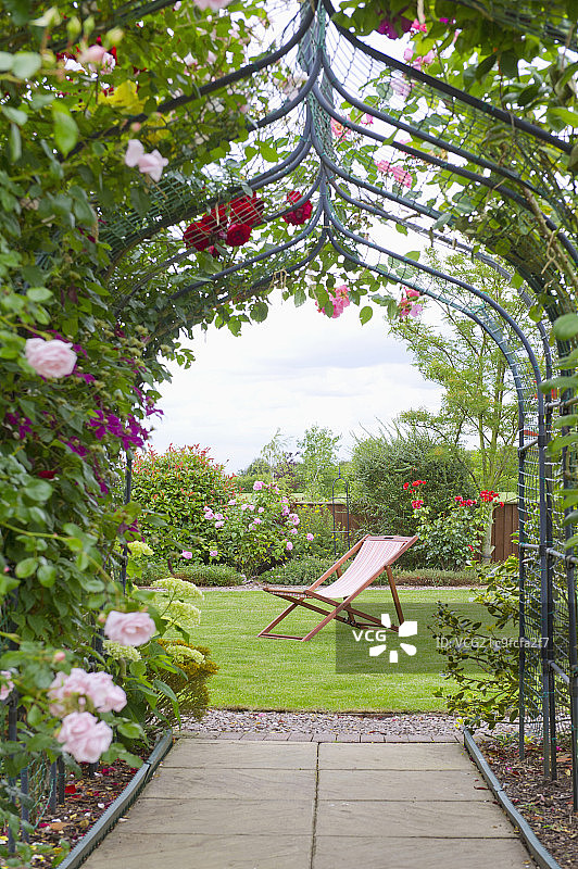 A garden with a rose arch, and a deck chair图片素材