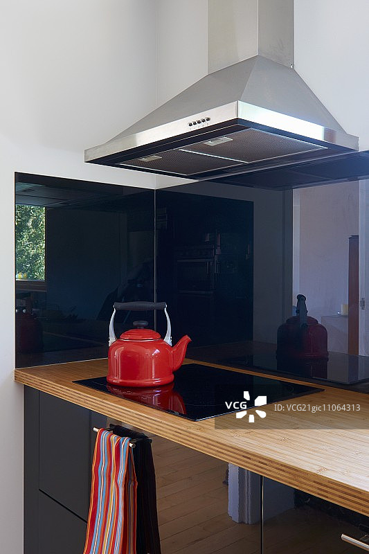 现代厨房的一角，黑色的橱柜门和黑色陶瓷铁架上的红色水壶图片素材
