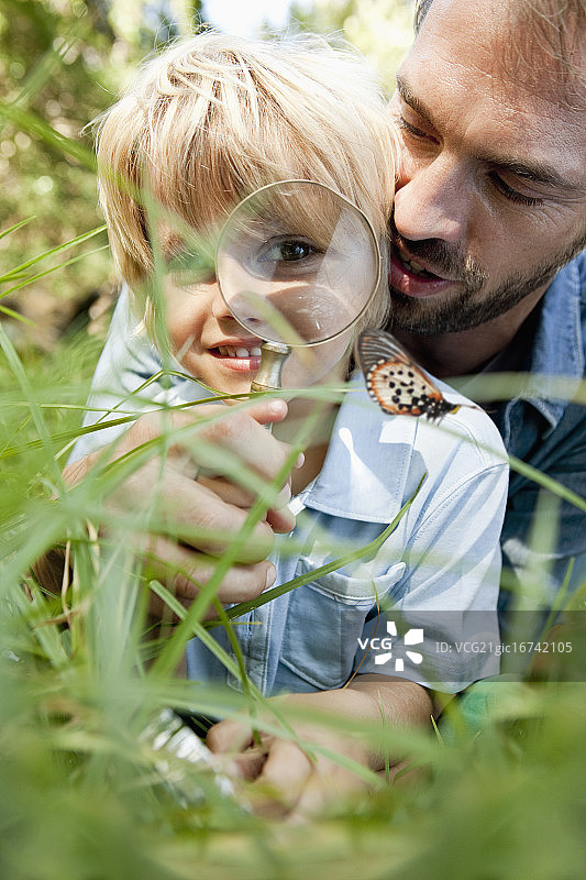 近距离的父亲与儿子(3-4)在大自然中通过放大镜看图片素材